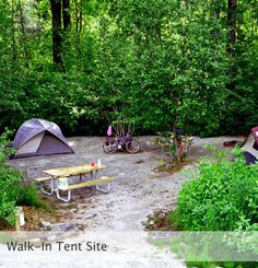 there are two tents in the woods with picnic tables and bikes parked next to them