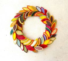 a colorful wreath made out of paper with leaves on it's sides, sitting on a white surface