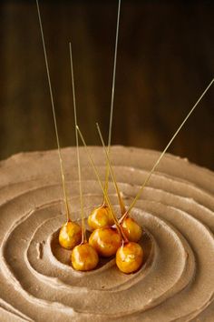 four small cherries sitting on top of a chocolate frosted cake with sticks sticking out of it