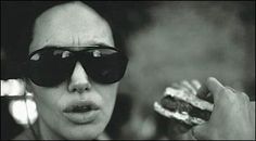 a black and white photo of a woman in sunglasses eating a sandwich with her hand