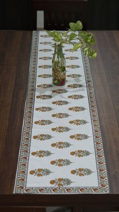 a table runner with flowers in a vase on top of it, sitting on a wooden table