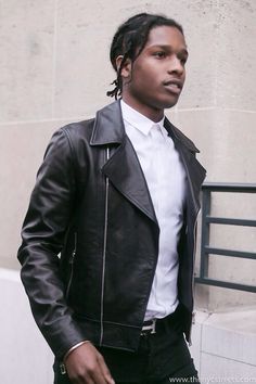 a man wearing a black leather jacket and white shirt standing in front of a building