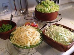 three bowls filled with food on top of a kitchen counter next to a bowl full of lettuce