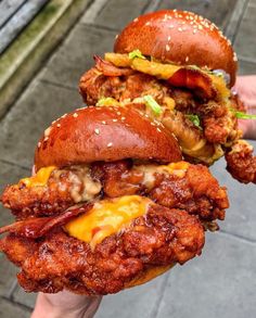 two sandwiches with meat and cheese are held up in the air by someone's hand