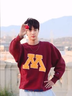 a young man wearing a maroon sweatshirt and white pants with his hands on his head