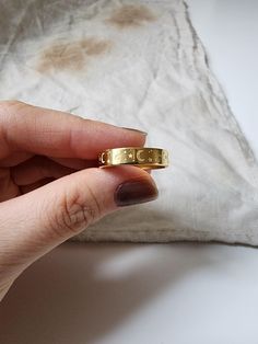 a hand holding a gold ring on top of a pillow