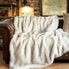 a large white fur blanket on top of a brown leather couch in front of a brick wall