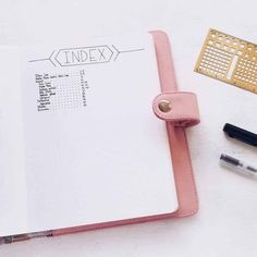 an open notebook sitting on top of a white table next to pens and pencils