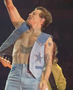 a shirtless man with an electric guitar in his right hand and one arm raised