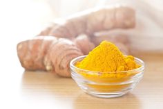 a glass bowl filled with yellow powder next to a ginger root on a wooden table