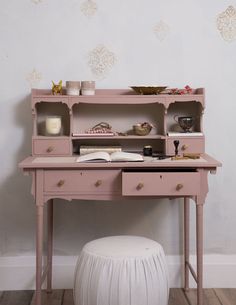 a pink desk with drawers and a white poufce stool in front of it