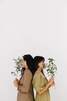 two women standing next to each other holding flowers