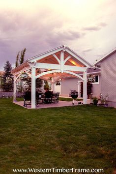 a covered patio with an outdoor dining table and grill area in the back yard at dusk