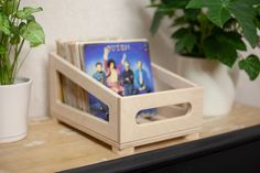 a wooden box with dvd's in it sitting on a shelf next to a potted plant