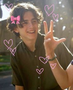 a young man making the peace sign with pink hearts drawn on his fingers in front of him