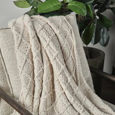 a white blanket sitting on top of a chair next to a potted plant