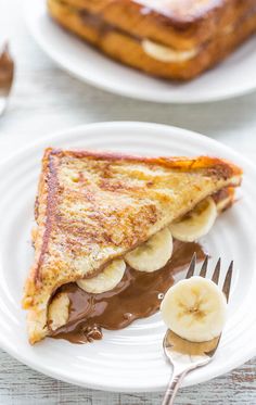 a slice of french toast with chocolate sauce and banana slices on a white plate next to a fork