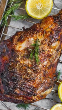 a piece of meat sitting on top of a metal rack next to lemons and rosemary