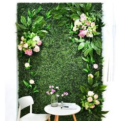 a table with two chairs next to a wall covered in greenery and pink flowers