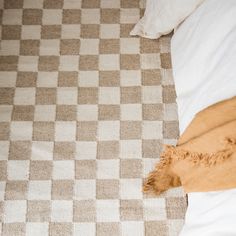 a brown and white checkered rug on top of a bed next to a pillow