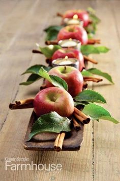 a row of apples with cinnamon sticks and green leaves on the side, sitting on a wooden table