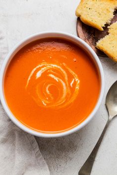 a bowl of tomato soup next to slices of bread