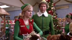 two people dressed as elfs and one is holding a teddy bear in a shopping cart