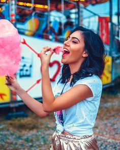 a woman is eating a pink lollipop in front of an amusement park ride