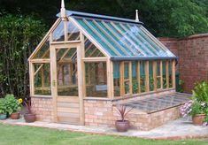 a small wooden greenhouse sitting on top of a lush green field next to a brick wall