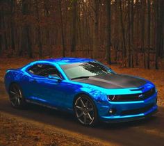 a blue camaro is parked on the side of a road in front of some trees