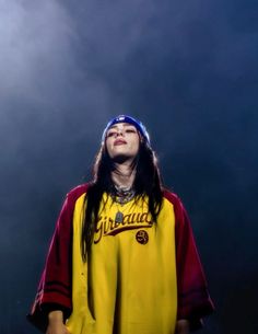 a woman with long hair wearing a yellow shirt and headband standing in front of a dark background