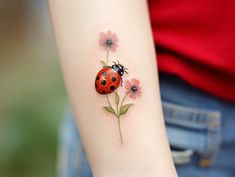 a ladybug tattoo on the arm with pink flowers and daisies around it