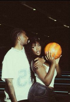 two people standing next to each other holding an orange