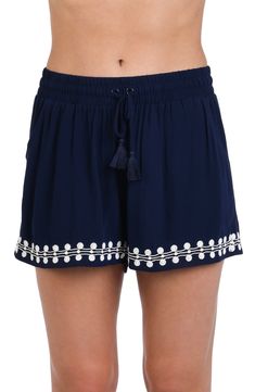 Model is wearing an indigo and white patterned beach shorts that resembles a string of white sea scallop shells. Bohemian Drawstring Shorts For Beach Season, Summer Beach Bottoms With Tassels, Summer Bottoms With Tassels For Beach Season, Casual Beach Bottoms With Tassels, Beachwear Bottoms With Tassels For Vacation, Vacation Beachwear Bottoms With Tassels, Summer Beachwear Bottoms With Tassels, Casual Embroidered Beach Shorts, Embroidered Blue Bottoms For Beach