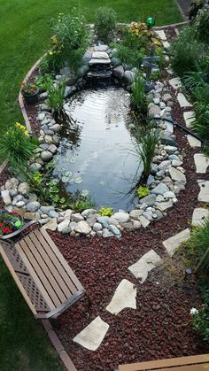 a small pond surrounded by rocks and gravel with a bench in the middle next to it