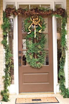 a christmas wreath on the front door of a house decorated with evergreen garland and pine cones