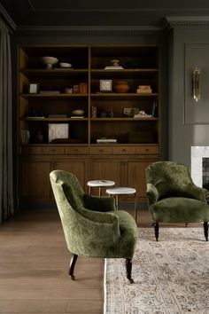 a living room with two green chairs and a rug in front of a bookcase