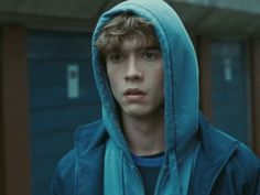 a young man wearing a blue hoodie and looking at the camera while standing in front of a building