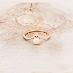 a gold ring with a pearl sits on a piece of wood