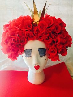 a white mannequin head with red flowers on it's head and a gold crown