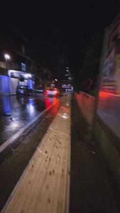 cars driving down the road at night with rain on the ground and street lights in the background