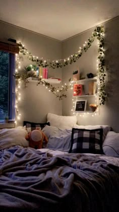 an unmade bed with christmas lights on the headboard