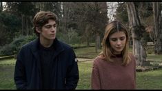 a young man and woman standing next to each other in front of trees with grass