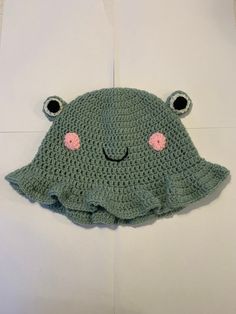 a green crocheted hat with pink eyes and ears on top of a white surface