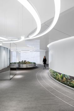 a woman is walking through an office building with circular walls and plants on the wall