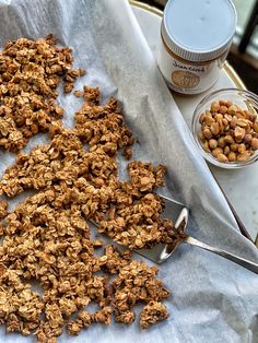 some granola on a table next to a spoon and bowl of nuts with yogurt in the background