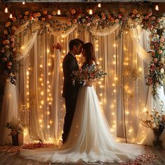 a bride and groom are standing in front of a backdrop with flowers, candles and fairy lights