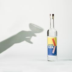 the shadow of a hand holding a bottle of gin in front of a white background