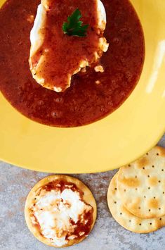 a yellow plate topped with food next to crackers and a bowl of soup on top of a table