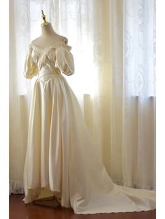 a white dress is on display in front of a window with curtains and drapes